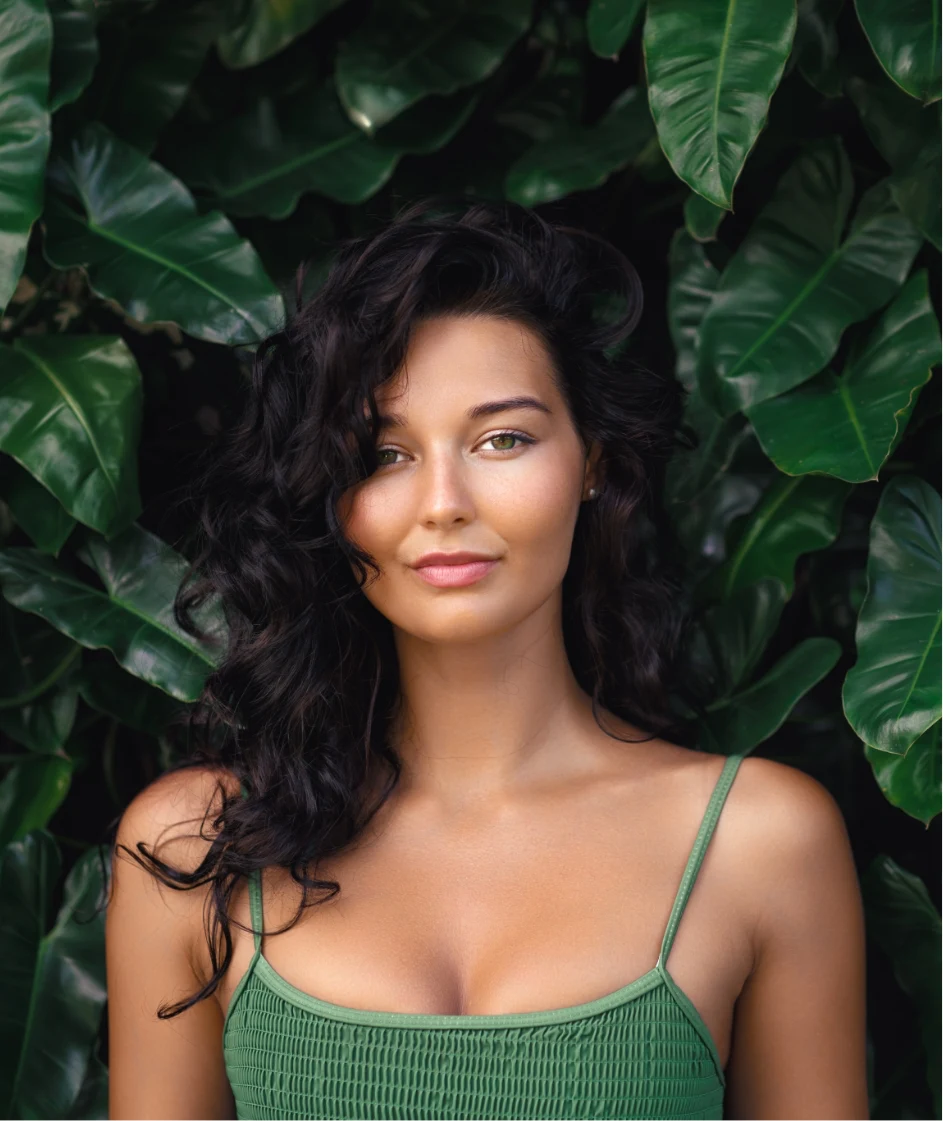 beautiful woman with perfect skin posing in front of tropical foliage